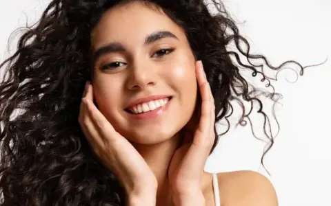 Sonrisa radiante con un toque de strawberry makeup, cabello rizado oscuro y piel luminosa.
