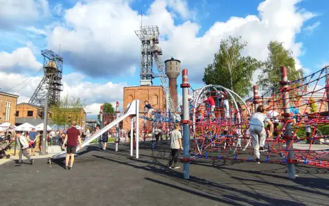 Rybnik atrakcje: plac zabaw dla dzieci z linowymi konstrukcjami i zjeżdżalnią, w tle wieże szybowe kopalni.