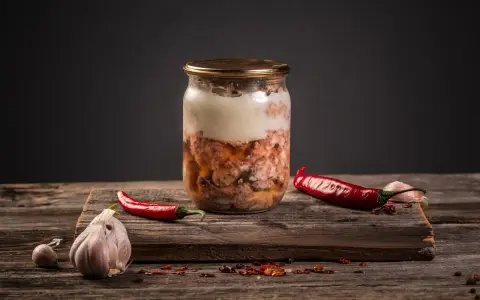 Słoik z mięsem, czosnek i papryczki chili. Przygotowanie tyndalizacji mięsa w piekarniku.