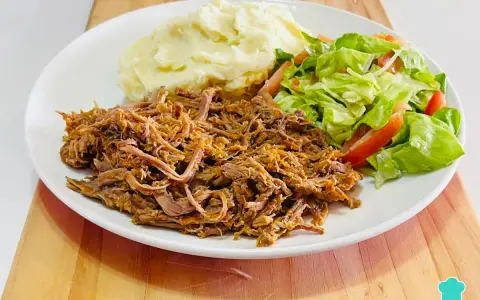 Plato de carne mechada jugosa, puré de papas cremoso y ensalada fresca de lechuga y tomate.