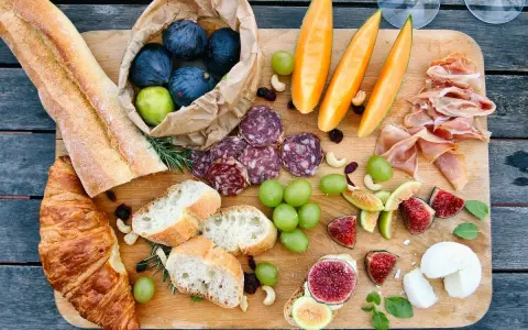 Tabla de quesos y embutidos: baguettes, croissants, higos, uvas, melón, jamón serrano y salami. Un festín que muestra qué comen los franceses.