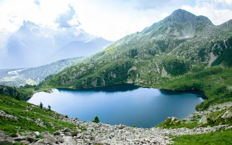 Un sereno lago ritorto incastonato tra montagne verdi e rocciose, con cime nebbiose all'orizzonte.