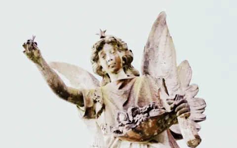 Kamienna figura anioła z gwiazdą na głowie, trzymająca w dłoniach kwiaty i gałązkę. Symbolika 2244 znaczenie.