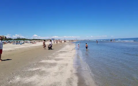 Una giornata di sole a Pinarella di Cervia mare, con bagnanti che passeggiano sulla sabbia e bambini che giocano nell'acqua cristallina.
