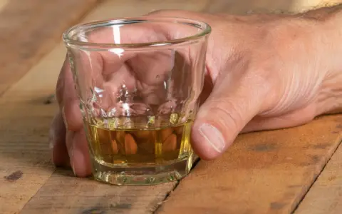 Dłoń trzyma kieliszek z bursztynowym płynem. Czy alkohol podnosi ciśnienie? To pytanie nurtuje wielu, gdy sięgają po taki trunek.