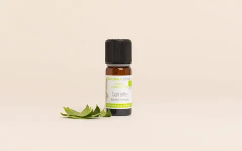 Flacon d'huile essentielle sarriette des montagnes, aux vertus purifiantes et toniques, accompagné de quelques feuilles fraîches.