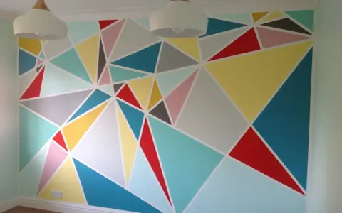 Kolorowe malunki na ścianie dla dzieci w geometryczne wzory. Radosna, pastelowa paleta barw tworzy wesołą atmosferę.