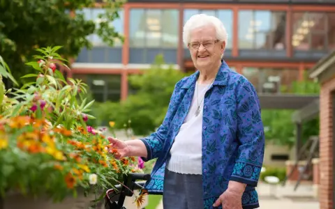 An elderly woman smiles, tending to flowers outside the St. Rose of Viterbo Convent.