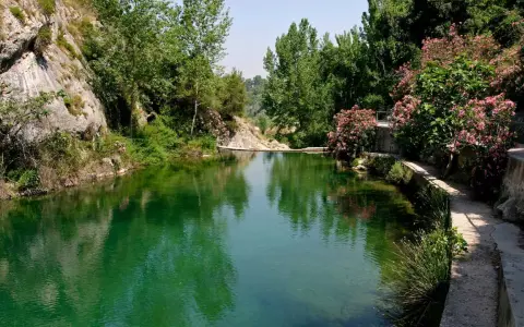 Un remanso de agua verde rodeado de rocas y vegetación exuberante. Un camino serpentea junto al agua, ideal para explorar qué ver en Ontinyent.