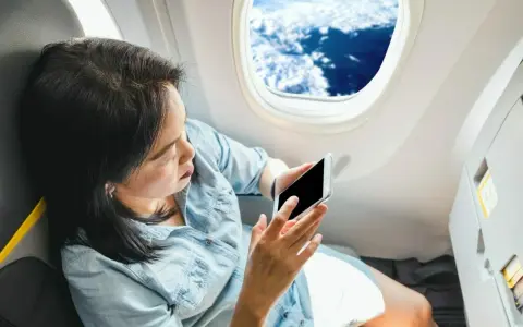 Kobieta z telefonem siedzi przy oknie w samolocie Ryanair, podziwiając chmury.