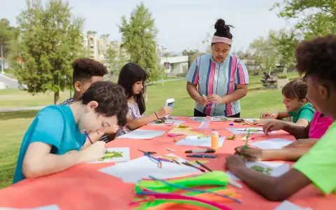 Des enfants créent des œuvres d'art en plein air autour d'une table recouverte d'une nappe orange.