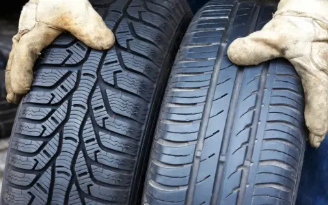 Zwei Reifen werden von Händen in Arbeitshandschuhen gehalten. Links ein Winterreifen, rechts ein Sommerreifen. Darf man mit Winterreifen im Sommer fahren?