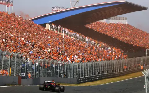 Un coche de Fórmula 1 compite en el Dutch Grand Prix ante una multitud masiva vestida de naranja.