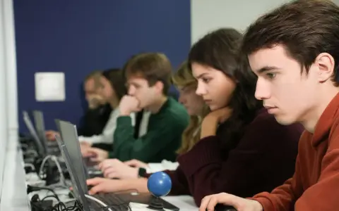Studenci podczas zajęć z informatyki w Katowicach, skupieni na ekranach laptopów.