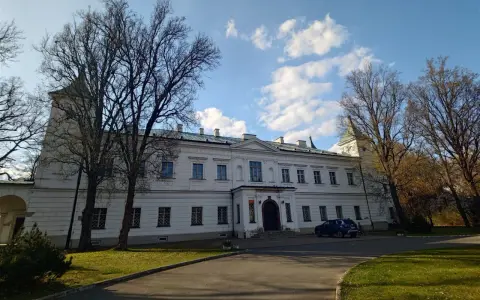 Pałac w Falentach, biała, okazała budowla z wieżyczką, otoczona drzewami o nagich gałęziach, pod błękitnym niebem z chmurami.