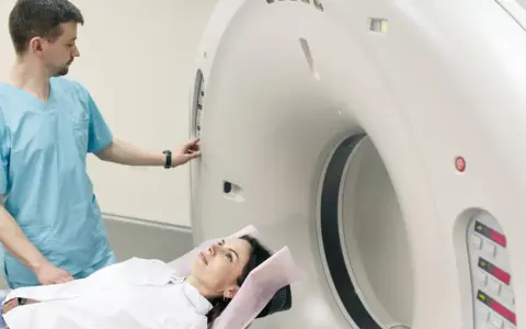 Pacjentka leży na stole do rezonansu, a technik przygotowuje aparat do badania. Rezonans całego organizmu co wykrywa? To zaawansowana diagnostyka obrazowa.
