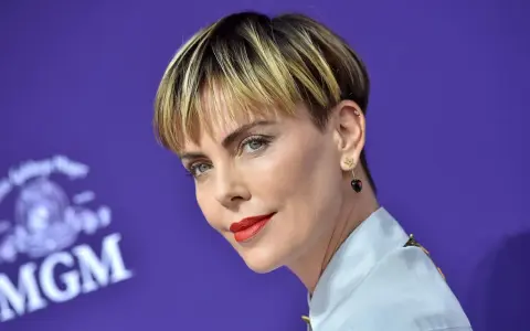 Charlize Theron mit fransigen Kurzhaarfrisuren Damen, rotem Lippenstift und Stern-Herz-Ohrringen vor MGM-Logo.