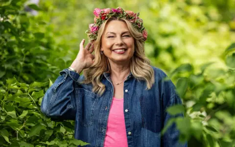Glad kvinna med blomsterkrans ler i grönska. Hon är årets sommarpratare och bär jeansskjorta.