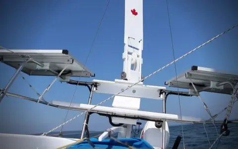 Weiße Windfahne mit kanadischer Flagge auf einem Segelboot, mit Solarpaneelen und dem blauen Himmel im Hintergrund.