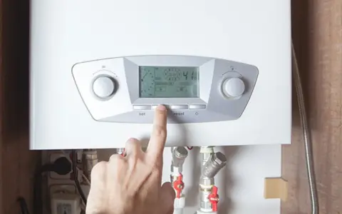 Un dedo presiona un botón en una caldera moderna, indicando el futuro de las calderas de gas y su control inteligente.