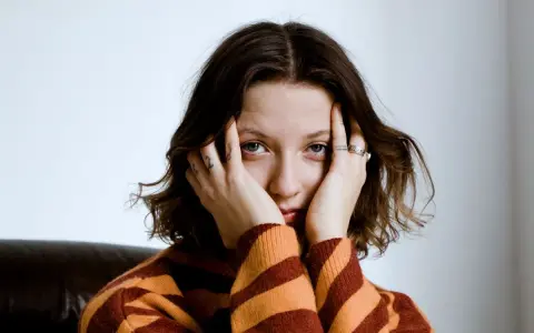 Justyna Święs Piernikowski w swetrze w pasy, z dłońmi przy twarzy, patrzy w obiektyw.