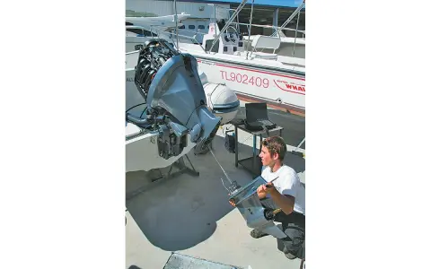 Un mécanicien examine une pièce de moteur hors-bord, suspectant un symptôme d'essence trop vieille. Un ordinateur portable est à proximité pour le diagnostic.