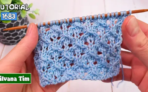 Manos tejiendo un patrón de puntos calados a dos agujas utilisima en hilo azul claro. El tejido muestra un diseño intrincado con agujeros y trenzas.
