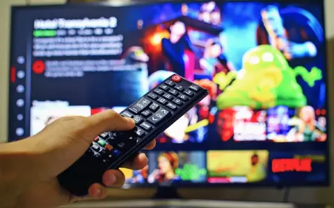 Dłoń trzymająca pilot do telewizora, na ekranie menu platformy streamingowej. Wady i zalety reklamy telewizyjnej – czy warto ją oglądać?