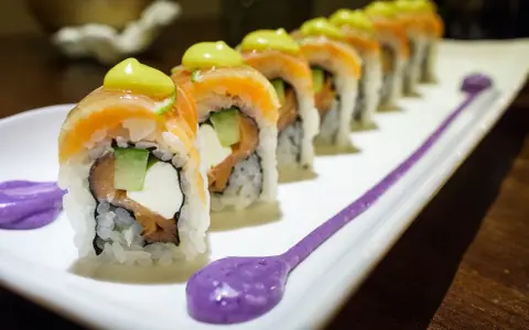 Une délicieuse recette maki original : rouleaux de saumon, avocat, concombre et fromage frais, ornés d'une touche de sauce verte et de purée violette.