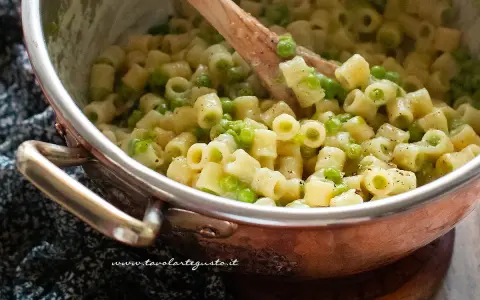 Un primo piatto invitante: pasta e piselli cremosa, mescolata con un cucchiaio di legno in una pentola di rame.