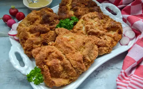 Goldbraun paniertes Schnitzel, perfekt zubereitet, liegt auf einem weißen Teller, garniert mit Petersilie und Radieschen.