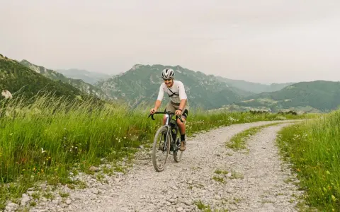 Kolarz na rowerze pokonuje krętą drogę z **gravel co to** w tle górskiego krajobrazu.