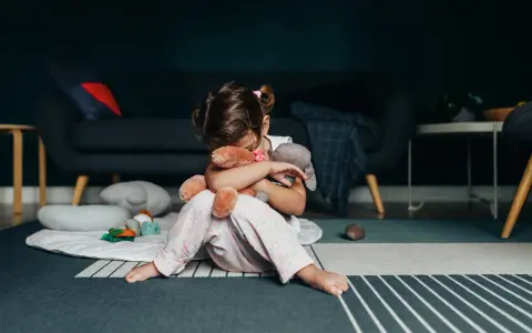 Smutna dziewczynka tuli misie, zastanawiając się nad przyczynami padaczki u dzieci.