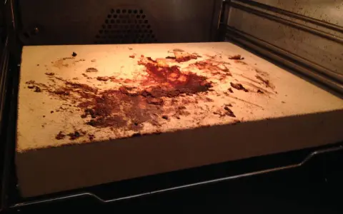 Ein schmutziger pizzastein mit braunen Flecken und Essensresten, der im Ofen liegt.