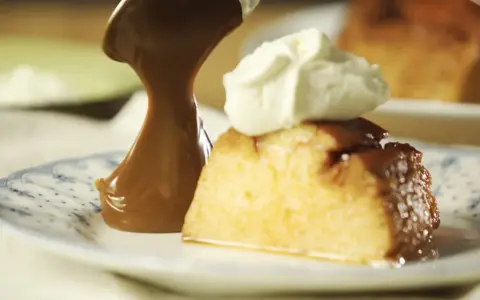 Un trozo de flan de 12 huevos, cubierto con caramelo y crema batida, servido en un plato con diseño azul.