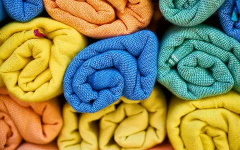 Rolled towels in vibrant colors: yellow, orange, blue, and green. These are made from biodegradable fabric, perfect for eco-conscious living.