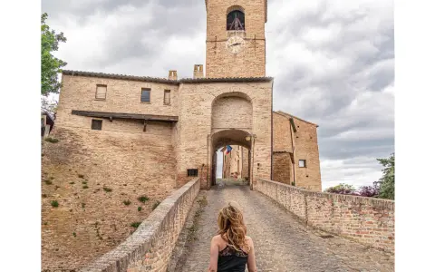 Passeggiata verso il borgo di Montegridolfo cosa vedere: un antico portale in mattoni con torre dell'orologio e un ponte acciottolato.