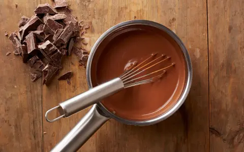 Chocolat fondu qui durcit dans une casserole, avec des morceaux de chocolat à côté sur une planche en bois.