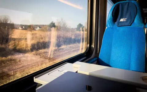 Podróż pociągiem z Katowic do Krakowa Balic. Widok z okna na krajobraz, obok niebieskie siedzenie i stolik z laptopem.