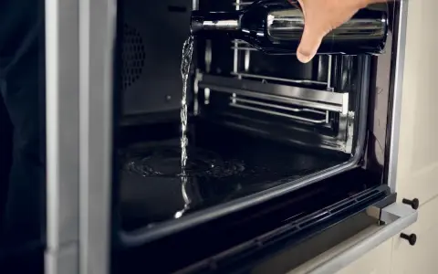 Wasser wird aus einer Flasche in einen modernen **Hydrolyse Backofen** gegossen, um die Reinigung zu erleichtern.