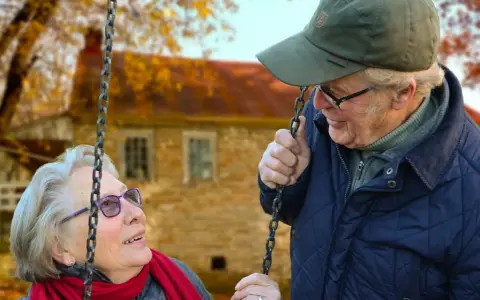 Aktywny seniorzy cieszą się jesiennym dniem na huśtawce. Uśmiechnięta para w otoczeniu złotych liści.