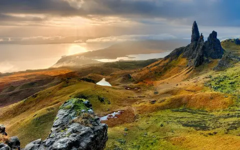 Paysage écossais spectaculaire, photo HDR. Des collines ondulantes aux teintes dorées et vertes, des lacs scintillants et des formations rocheuses imposantes sous un ciel dramatique.