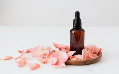 Flacon d'huile essentielle ambré entouré de pétales de rose. Un soin doux pour une femme enceinte.