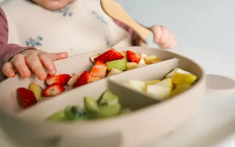 Bebé explorando fresas, kiwi y plátano en su plato. Es un buen momento para ofrecer fruta a los bebés.