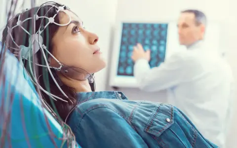 Kobieta w czepku EEG podczas badania VEP. Lekarz analizuje wyniki na ekranie.
