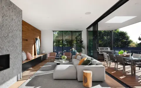 Elegante salón con chimenea de piedra, pared de madera y grandes ventanales que conectan con una terraza. Un ejemplo de las últimas tendencias interiorismo.