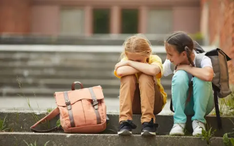 Dziewczynka płacze, jej koleżanka ją pociesza. To obraz pokazuje, jak **znęcanie się psychiczne w szkole konsekwencje** może mieć dla dzieci.