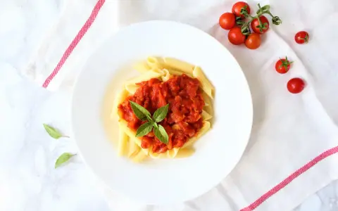 Penne z sosem pomidorowym i bazylią, obok świeże pomidorki koktajlowe.