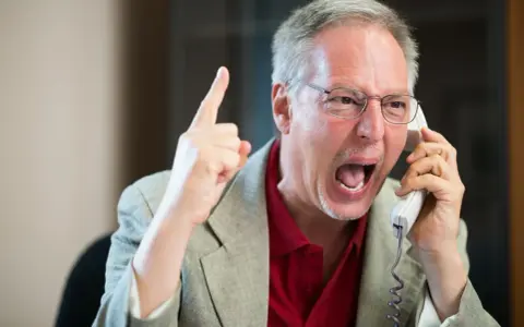 Mężczyzna z labilnością emocjonalną krzyczy do telefonu, unosząc palec wskazujący w geście ostrzeżenia.