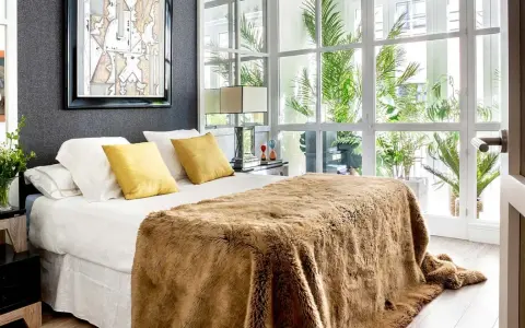 Cama acogedora con manta peluda, cojines amarillos y arte abstracto. Un diseño moderno para decorar habitación con luz natural.